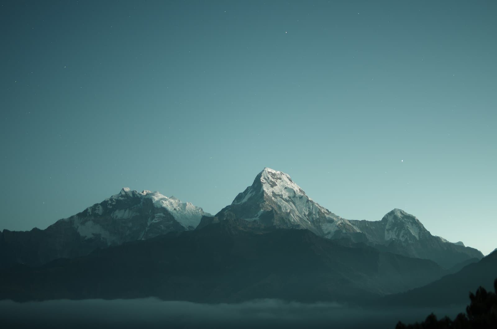 A moody teal mountain ridge under a dusk sky scattered with stars